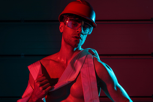 sexy shirtless fireman in protective helmet holding fire hose in darkness