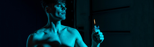 panoramic shot of sexy shirtless man holding lighter with closed eyes in darkness