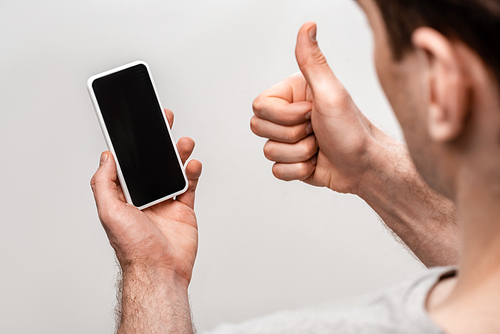 partial view of man showing thumb up while holding smartphone with blank screen isolated on grey