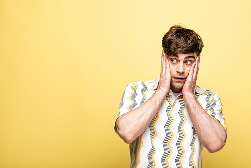 discouraged young man looking away and holding hand near face on yellow background