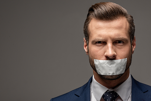 handsome businessman in suit with duct tape on mouth on grey with copy space