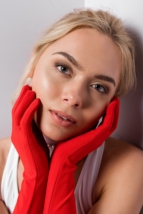 pretty blonde woman in red gloves touching face on white