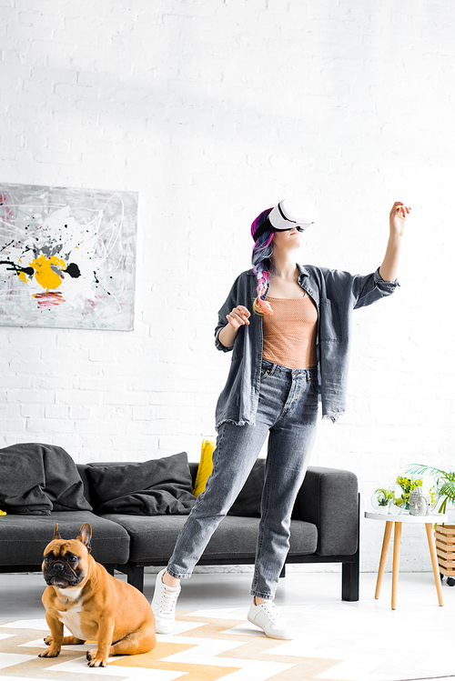 girl with colorful hair and VR headset standing near dog and gesturing in living room