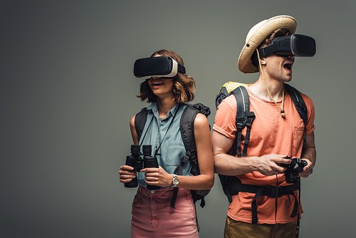 two excited tourists with binoculars and digital camera using virtual reality headsets on grey background