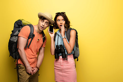 shocked young woman holding smartphone with blank screen near thoughtful man on yellow background