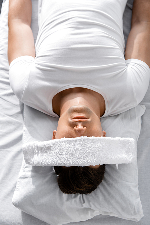 top view of young man with towel on eyes lying on pillow