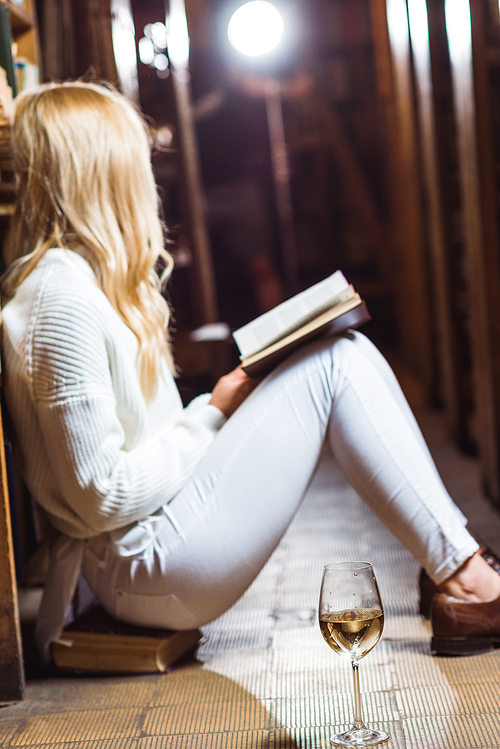 side view of blonde woman reading book and sitting on floor in library