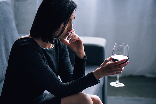 depressed woman sitting on sofa with wine glass at home