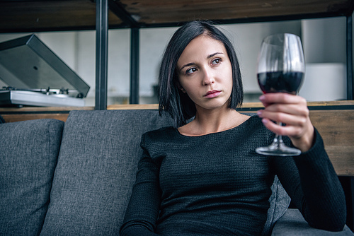 depressed woman on couch looking at wine glass at home