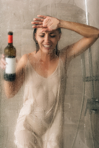 lonely depressed woman holding wine bottle, touching glass door and crying in shower