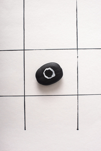 top view of tic tac toe game with black pubble marked with naught on white paper