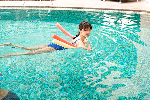 Side view of young woman  while swimming with pool noodles in swimming pool