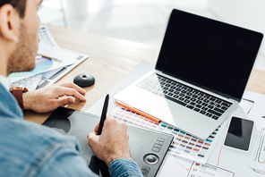 Selective focus of ux designer using laptop and graphics tablet near sketches and smartphone on table