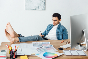 Barefoot designer using graphics tablet near sketches of user experience design and computer on table