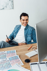 Smiling ux designer using graphics tablet and computer near color palettes on table