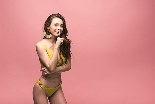 smiling 20대 여성 in yellow swimsuit showing hush sign isolated on pink