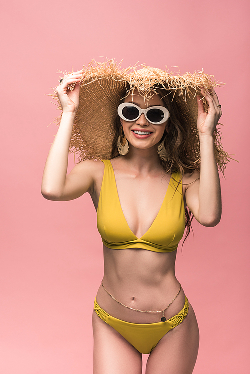 charming woman in straw hat and sunglasses smiling isolated on pink