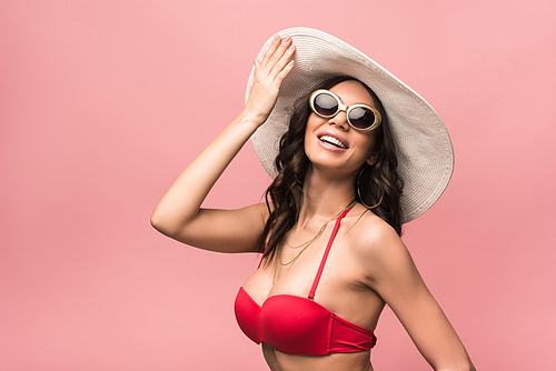 happy woman in sunglasses and hat smiling isolated on pink