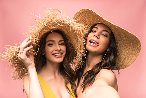 two smiling womans in straw hats taking selfie isolated on pink