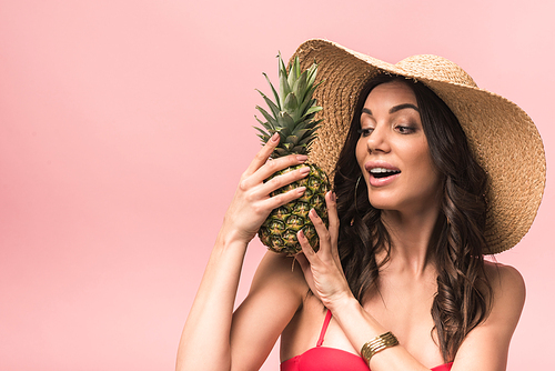 amazed 20대 여성 in straw hat and bikini holding pinapple isolated on pink