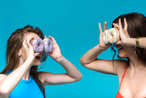 two girls in swimsuits holding donuts isolated on blue