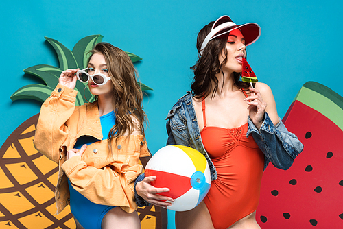 two girls with beach ball and lollipop near decorative watermelon and pineapple isolated on blue