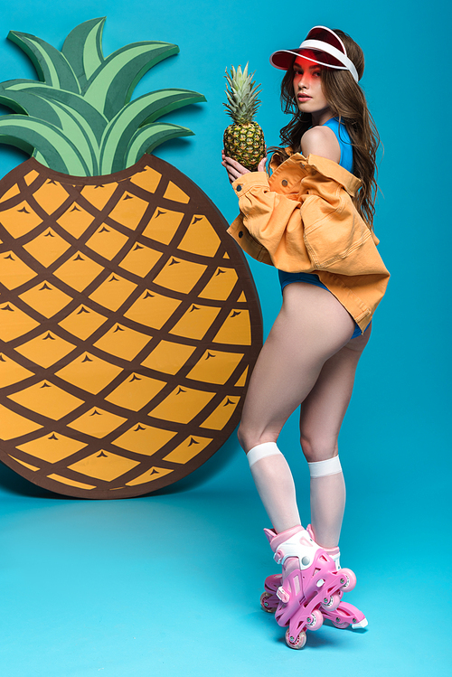 full length view of sexy girl in roller skates holding pineapple on blue