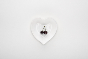 top view of red and fresh cherries on heart shaped white plate