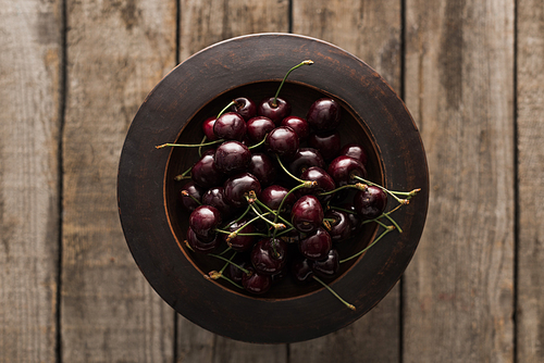 top view of red, fresh, whole and ripe cherries on bowl on wooden surface