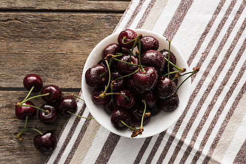 top view of fresh, whole and ripe cherries covered with droplets on bowl