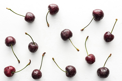 top view of fresh, whole and ripe cherries covered with water drops on white background
