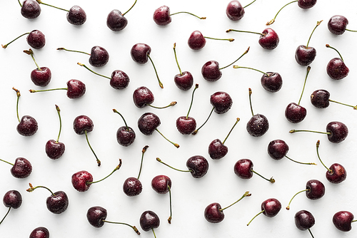 top view of red, whole and ripe cherries covered with water drops on white background