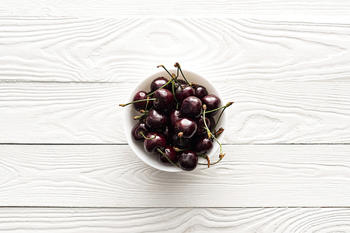 top view of fresh, sweet and ripe cherries on bowl on wooden background
