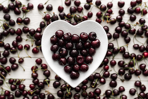 top view of fresh, sweet and ripe cherries covered with water drops on heart shaped plate