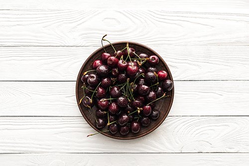 top view of fresh, sweet and wet cherries on plate on wooden background