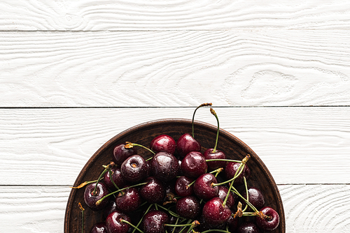 top view of fresh, sweet and washed cherries on plate on wooden background