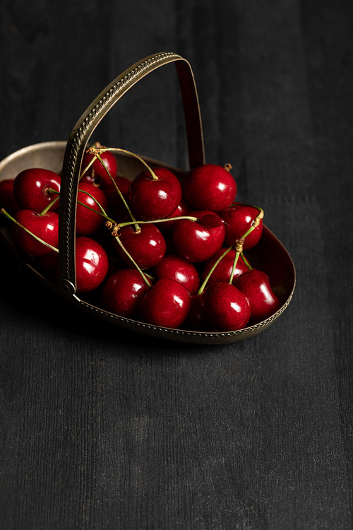 red delicious cherries in metal basket on wooden dark table