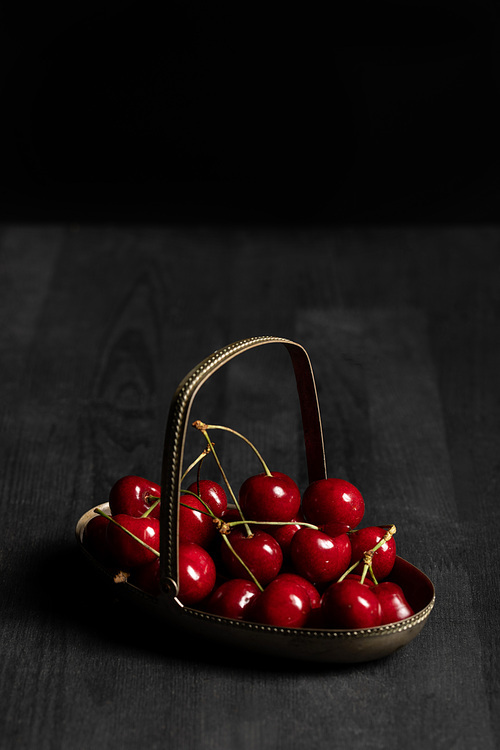 red delicious cherries in metal basket on wooden dark table isolated on black