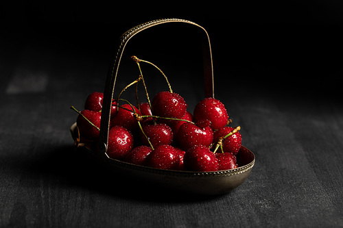 red delicious wet cherries in metal basket on wooden dark table isolated on black