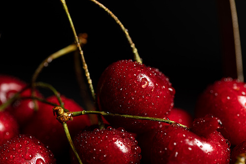 close up view of red delicious cherries with water drops isolated on black