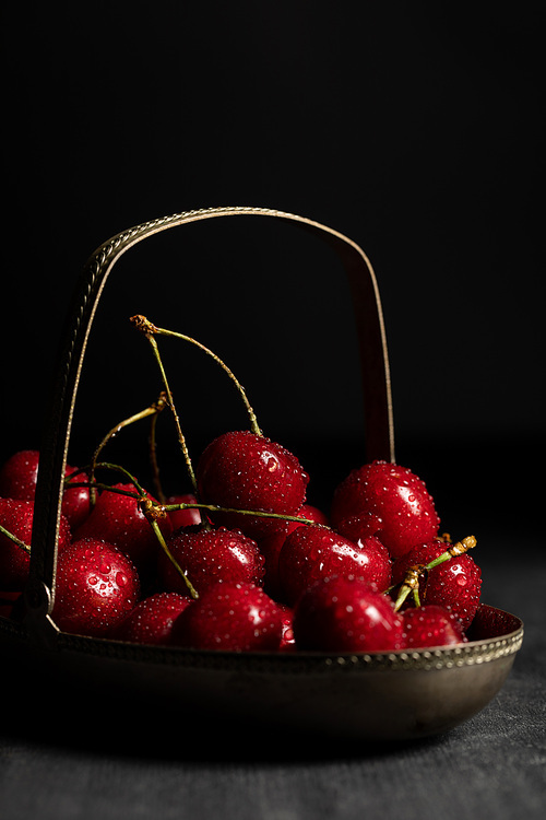 red delicious cherries with water drops in metal basket on wooden dark table isolated on black