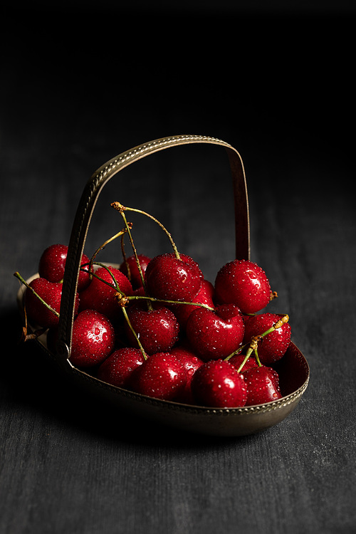 red tasty wet cherries in metal basket on wooden dark table isolated on black