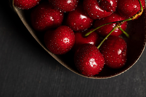 top view of wet delicious cherries in metal basket on wooden dark table