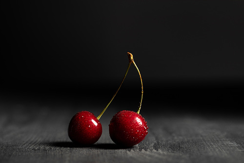 red delicious cherries with water drops on wooden table isolated on black