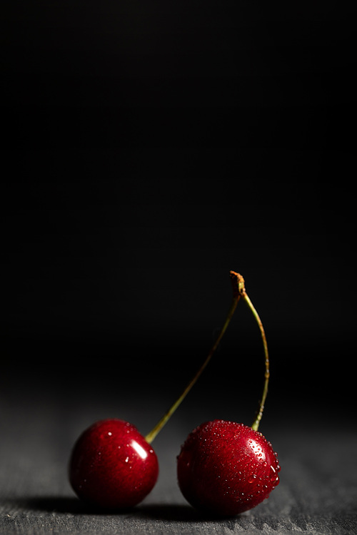 close up view of red delicious cherries with water drops on wooden table isolated on black