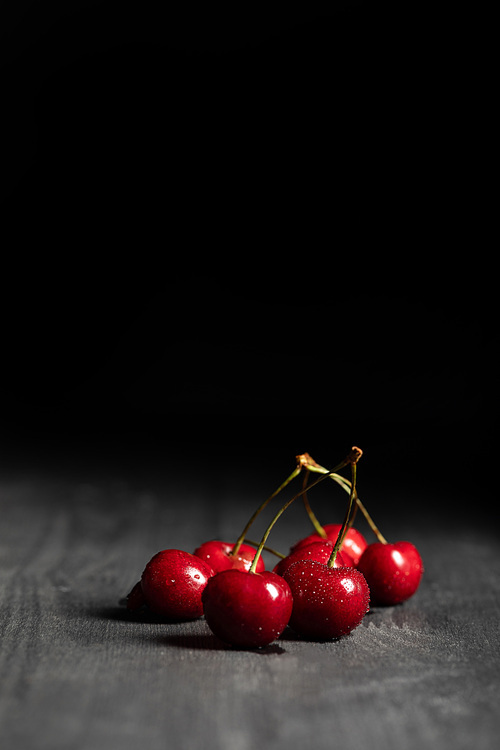 red tasty cherries with water drops on wooden table isolated on black