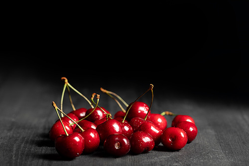 red delicious and ripe cherries on wooden dark table isolated on black