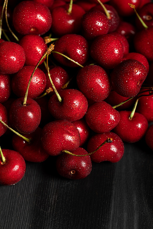close up view of red delicious and ripe cherries with water drops on wooden table