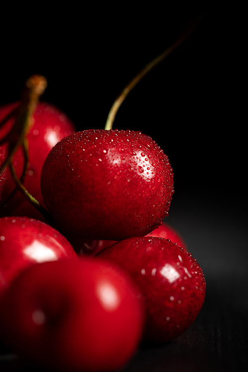 close up view of red tasty and ripe cherries with water drops on black background