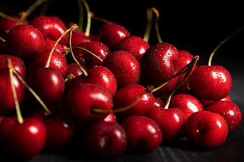 selective focus of red ripe cherries with water drops isolated on black